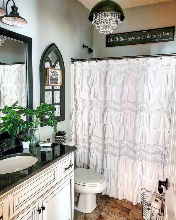 Bathroom with white ruffled shower curtain, green plants, and black countertop accents.