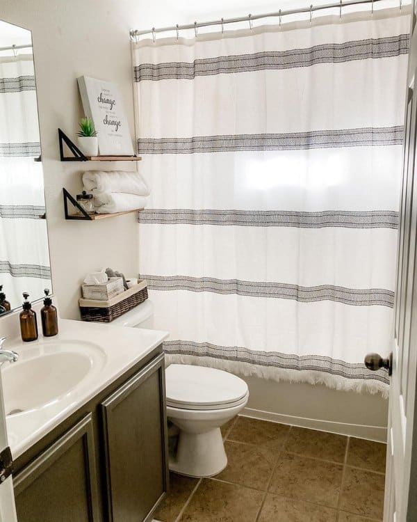 Simple bathroom with white and grey striped shower curtain, floating shelves, and neutral decor.