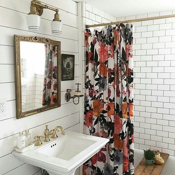 Bathroom with floral shower curtain, brass fixtures, and white subway tile walls.