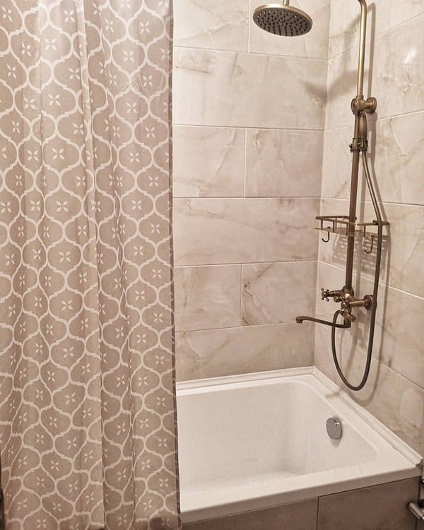 Shower area with patterned beige curtain, marble tiles, and brass fixtures.