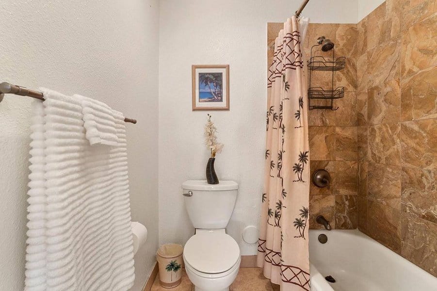 Bathroom with palm tree shower curtain, white towels, and brown tile bathtub area.