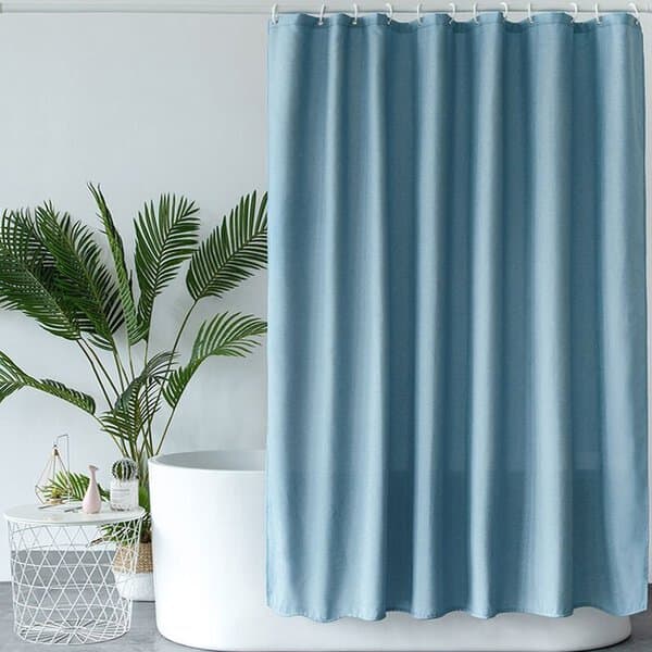 Light blue shower curtain in a minimalist bathroom with a potted plant and white freestanding tub.