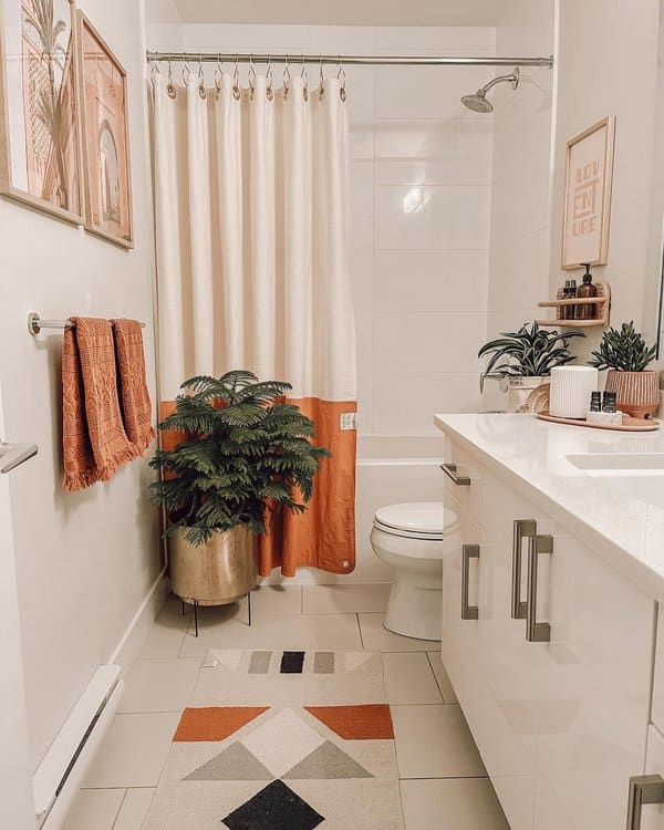 Small bathroom with a white and orange shower curtain, potted plant, and geometric rug.