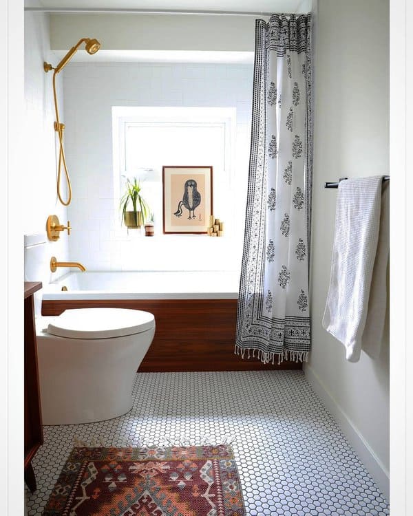 Small bathroom with black and white patterned shower curtain, gold fixtures, and mosaic floor tiles.