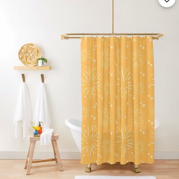 Golden yellow shower curtain with starburst pattern in a minimalist bathroom with white towels.