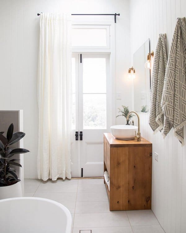 Minimalist bathroom with wooden vanity, white curtains, and freestanding tub.