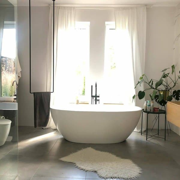 Bright bathroom with freestanding tub, white curtains, and indoor plants.