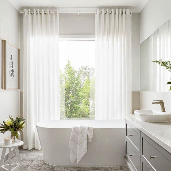 Bright bathroom with a freestanding tub, large window, and sheer white curtains.