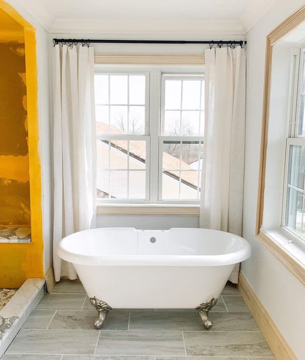 Bathroom with a clawfoot tub, large windows, and white curtains on a black curtain rod.