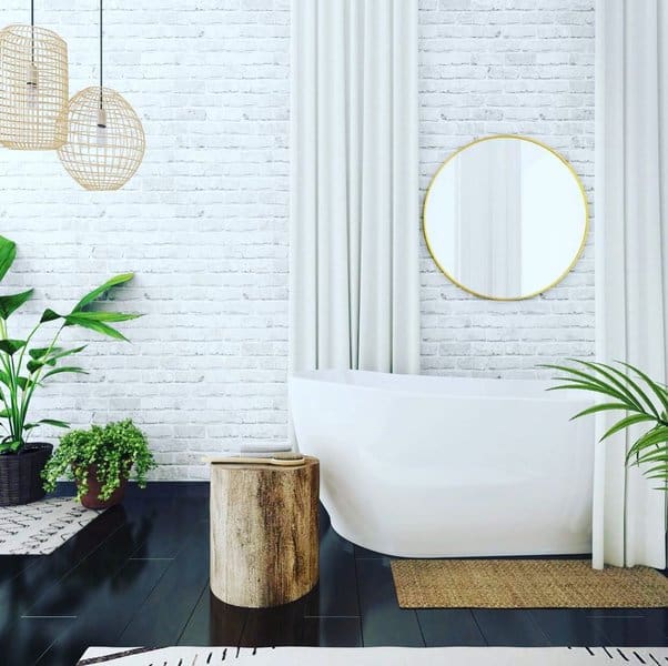 Modern bathroom with white brick wall, freestanding tub, white curtains, and green plants.