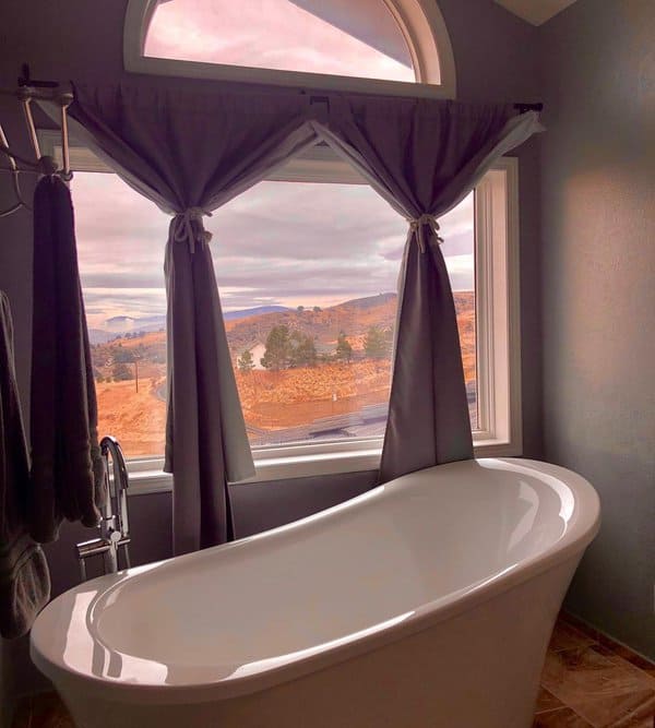 Freestanding tub with grey curtains framing a large window with scenic mountain views.