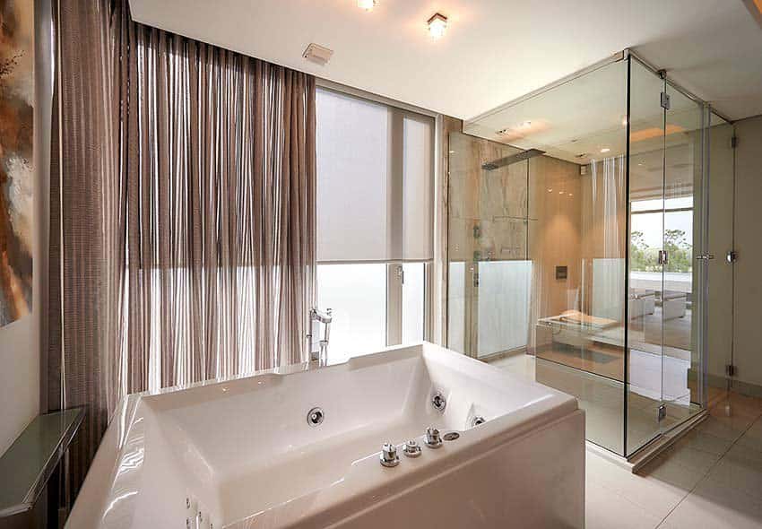 Modern bathroom with large windows, sheer curtains, and a jacuzzi tub next to a glass shower.