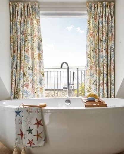 Freestanding tub with ocean view, colorful floral curtains, and a starfish-themed towel.