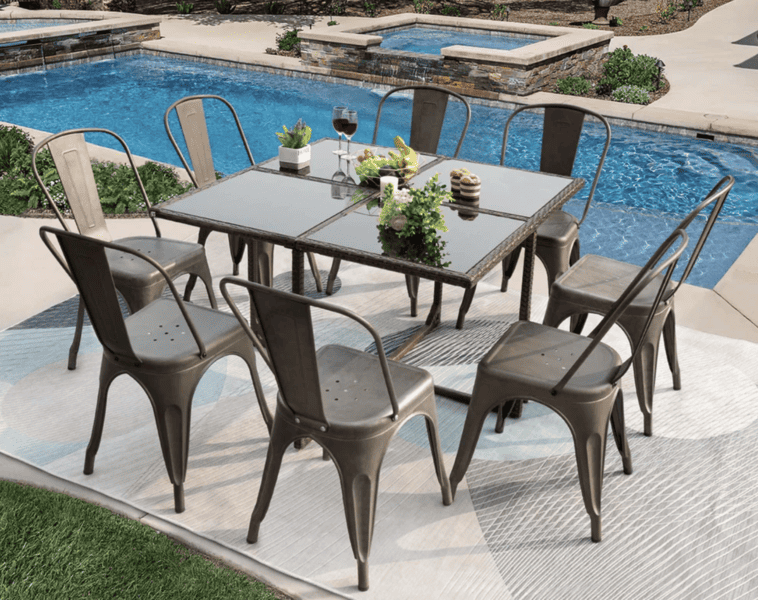 Metal outdoor dining set with a glass-top table and eight chairs by a poolside on a patterned rug.