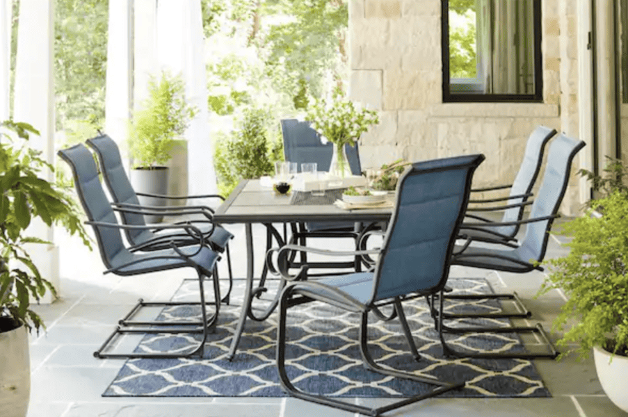 Outdoor dining set with blue cushioned chairs, a rectangular table, and a patterned rug on a patio.