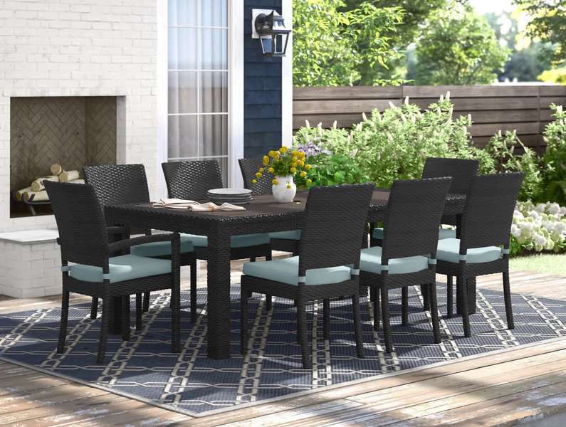 Outdoor dining set with wicker chairs and a rectangular table on a patterned rug near a fireplace.