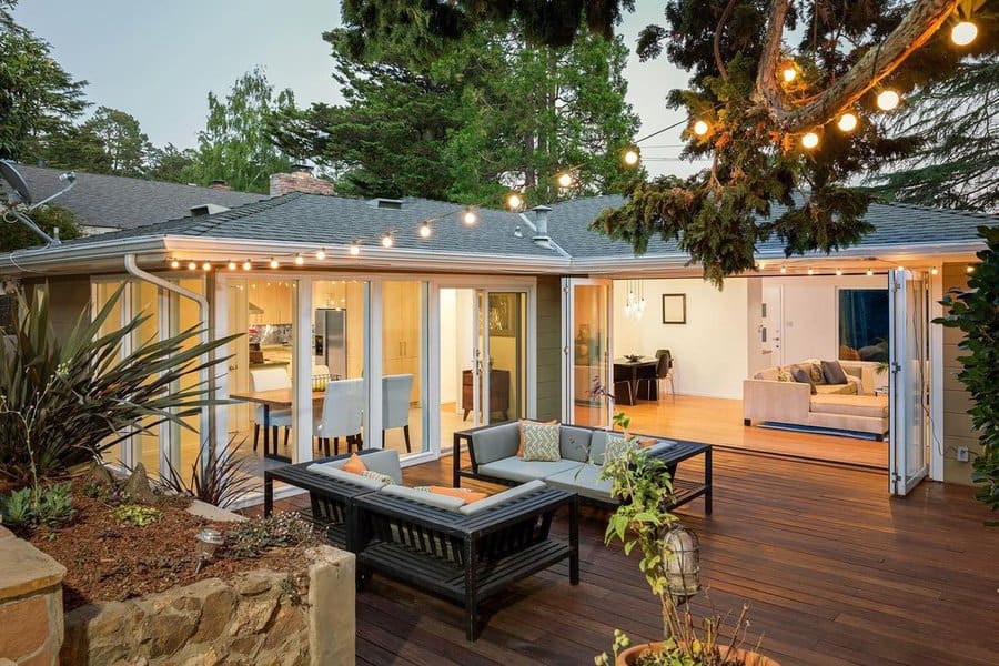 Elegant wooden deck with cozy seating, string lights, and open sliding doors connecting the outdoor space to a bright modern interior