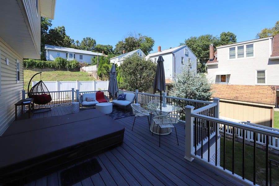 Spacious backyard deck with a hot tub, modern seating, umbrellas, and a hanging egg chair, offering a relaxing outdoor retreat