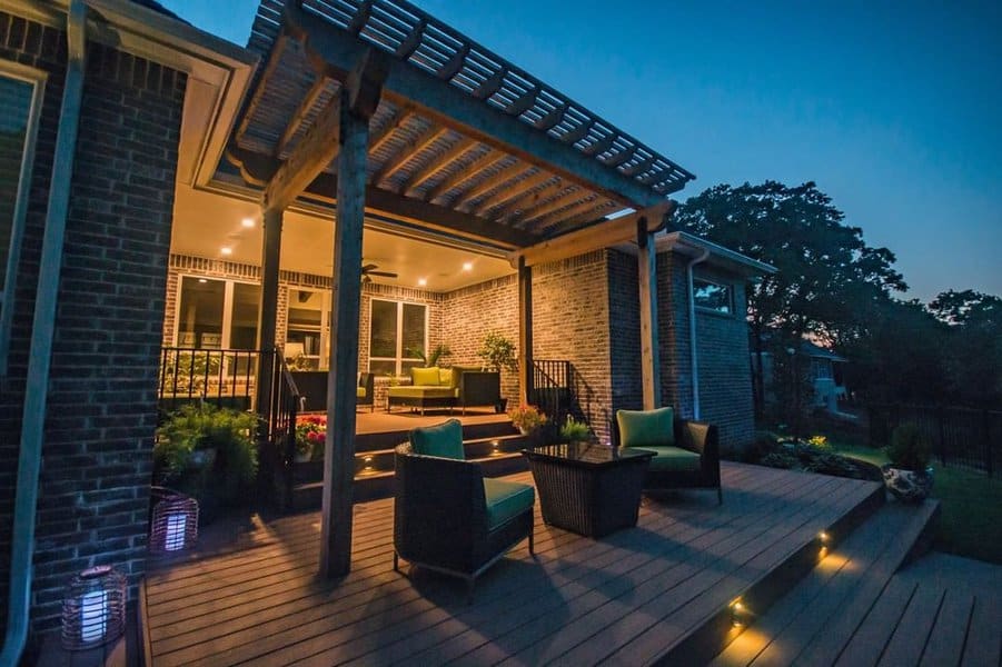 Modern backyard deck with a pergola, ambient lighting, wicker furniture, and a cozy indoor-outdoor transition under the evening sky