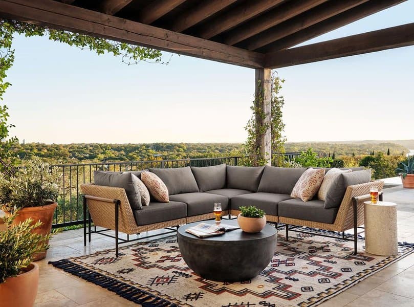 Elegant outdoor lounge with a sectional sofa, tribal-patterned rug, and scenic views under a wooden pergola