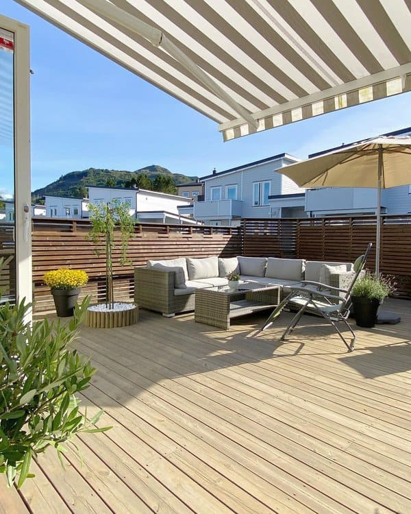 Spacious rooftop deck with comfortable wicker seating, striped awning, and serene mountain views, perfect for sunny relaxation