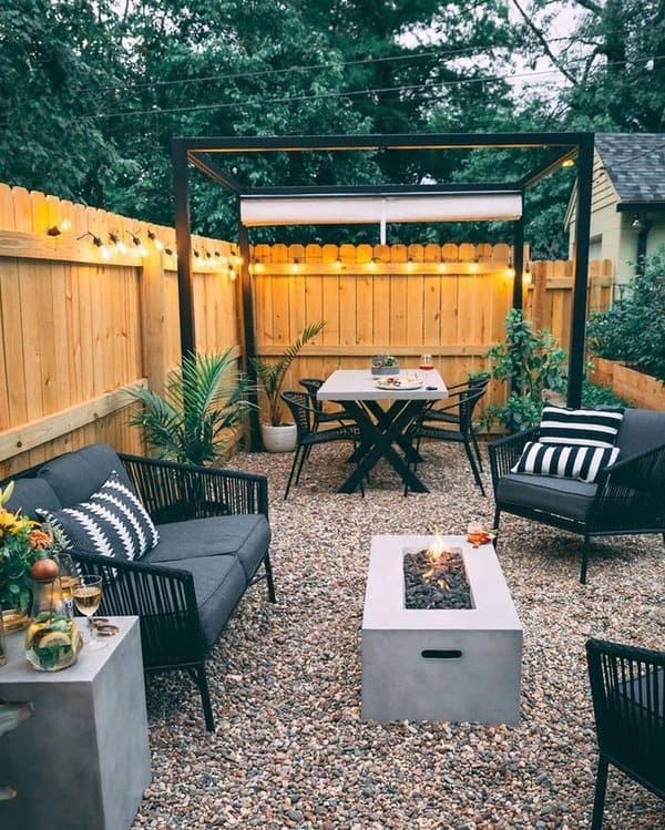 Cozy backyard oasis with string lights, sleek black furniture, and a modern fire pit centerpiece on a gravel floor