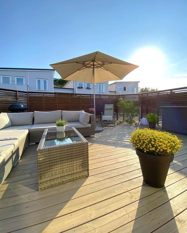 Modern patio with wicker seating, a glass-top coffee table, and a large umbrella for shade, complemented by vibrant yellow flowers in a planter