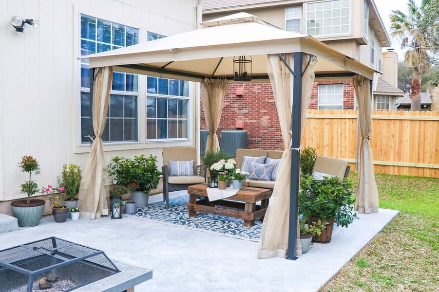 Stylish backyard patio with cozy wooden seating, vibrant flowers, a large umbrella for shade, and warm string lights for ambiance