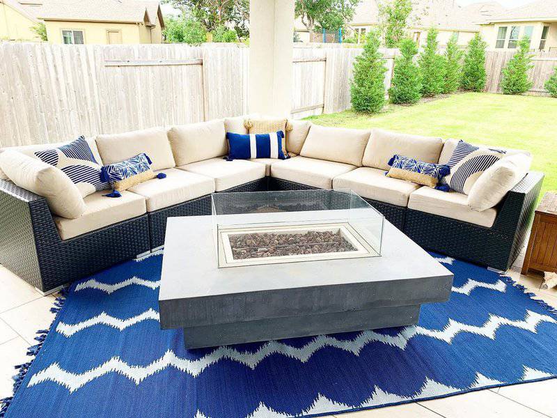 Modern patio setup with a sectional sofa, a sleek glass firepit, and a bold blue patterned rug for a vibrant outdoor retreat