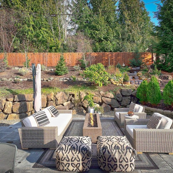 Elegant outdoor seating area featuring woven rattan sofas with white cushions and black-and-white striped pillows, arranged around a sleek rectangular firepit