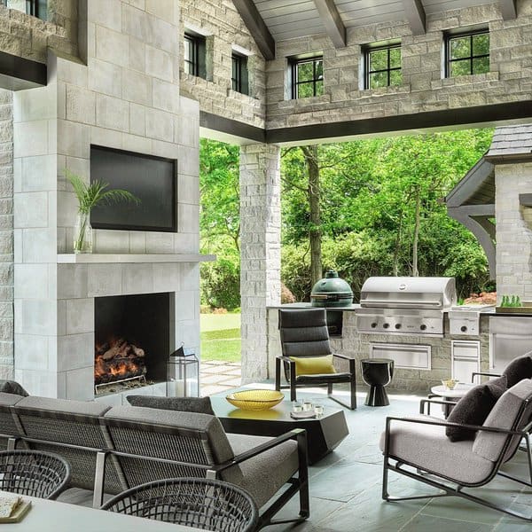 Modern outdoor lounge with a stone fireplace, built-in grill, and sleek gray seating under a vaulted ceiling