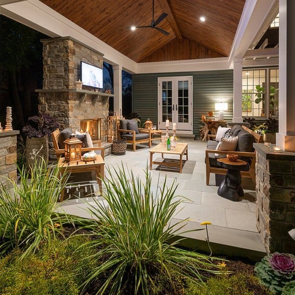 Cozy covered patio featuring a stone fireplace, wooden ceiling, ambient lighting, and stylish wooden seating for evening relaxation