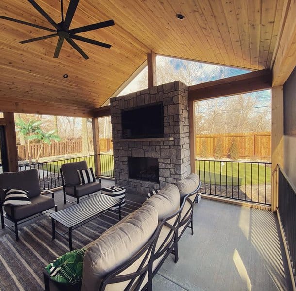 Modern outdoor room with a vaulted wooden ceiling, stone fireplace, and cozy seating for year-round comfort and relaxation