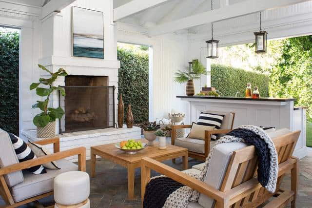 Charming outdoor living space with a white brick fireplace, wooden furniture, and lush greenery for a relaxing ambiance