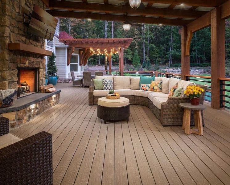 Spacious outdoor deck featuring a stone fireplace, cozy sectional seating, and warm string lights under a wooden pergola