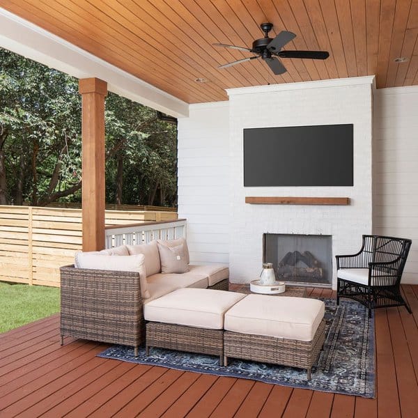 Modern patio with a white brick fireplace, wicker sectional seating, and a mounted TV under a wooden ceiling