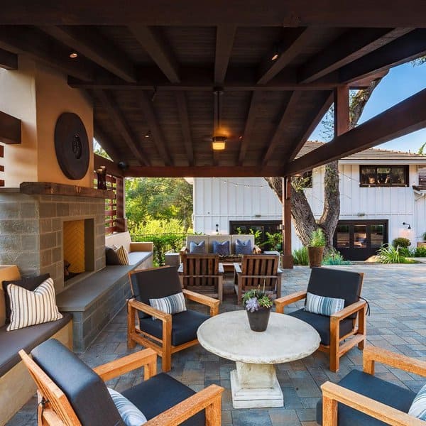 Modern outdoor patio featuring a dark wooden pergola, a sleek stone fireplace, and a mix of wooden and cushioned seating arranged around a circular centerpiece table