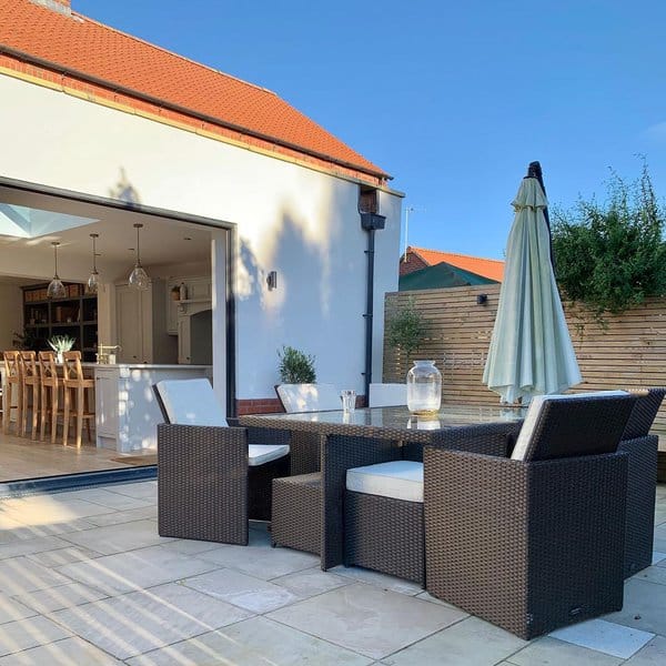 Modern outdoor dining area with a sleek wicker table set, cozy cushions, and an umbrella for shade, seamlessly connected to the indoor kitchen through sliding glass doors