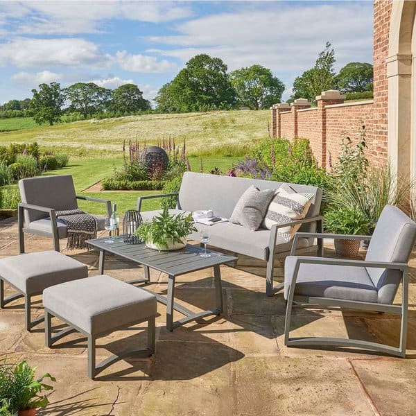 Elegant outdoor seating area with modern gray cushions, metal frames, and a lush garden backdrop, perfect for relaxing in the sun or entertaining guests