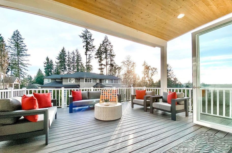 Modern outdoor deck with sleek furniture, vibrant red accent pillows, and a cozy central coffee table, offering serene views of the surrounding trees and neighborhood