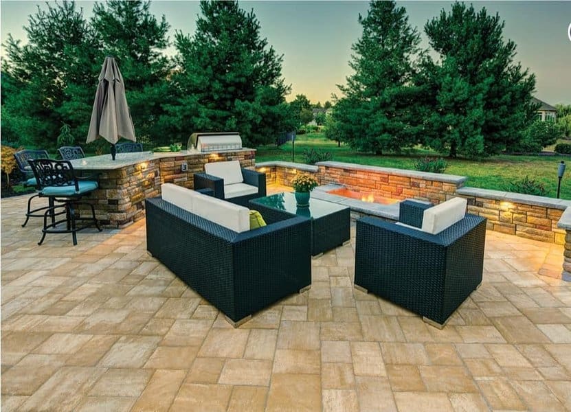 Stylish outdoor patio with wicker furniture, a stone bar, built-in grill, and ambient lighting surrounded by lush greenery