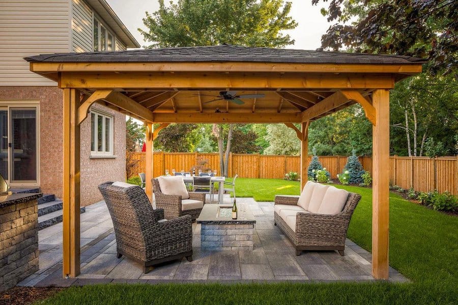 Cozy backyard gazebo with wicker seating, a fire table, and a lush green lawn framed by a wooden fence for a relaxing retreat