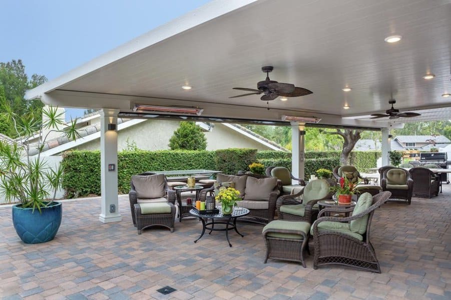 Spacious covered patio with wicker furniture, ceiling fans, ambient lighting, and a lush garden backdrop for outdoor entertaining