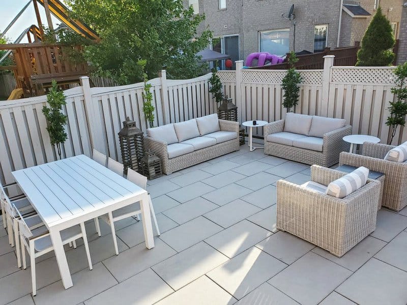 Modern patio with wicker furniture, white dining table, potted greenery, and a fenced backdrop for a private outdoor gathering space