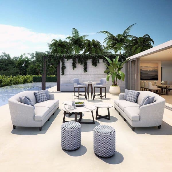 Luxurios outdoor living area featuring plush seating, chic side tables, and lush greenery by a serene poolside retreat