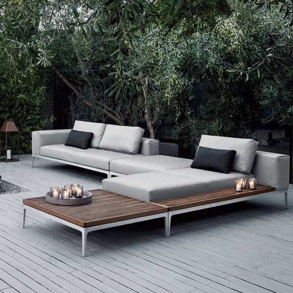 Modern outdoor lounge with sleek sofas, a wooden coffee table, and ambient candles, surrounded by lush greenery