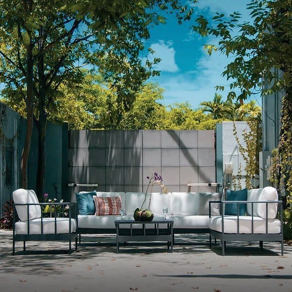 Contemporary outdoor seating area with sleek metal-framed furniture, white cushions, and vibrant accent pillows under lush greenery