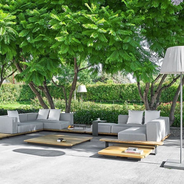 Serene outdoor space featuring a minimalist sectional, wooden tables, and lush greenery for a tranquil and modern retreat