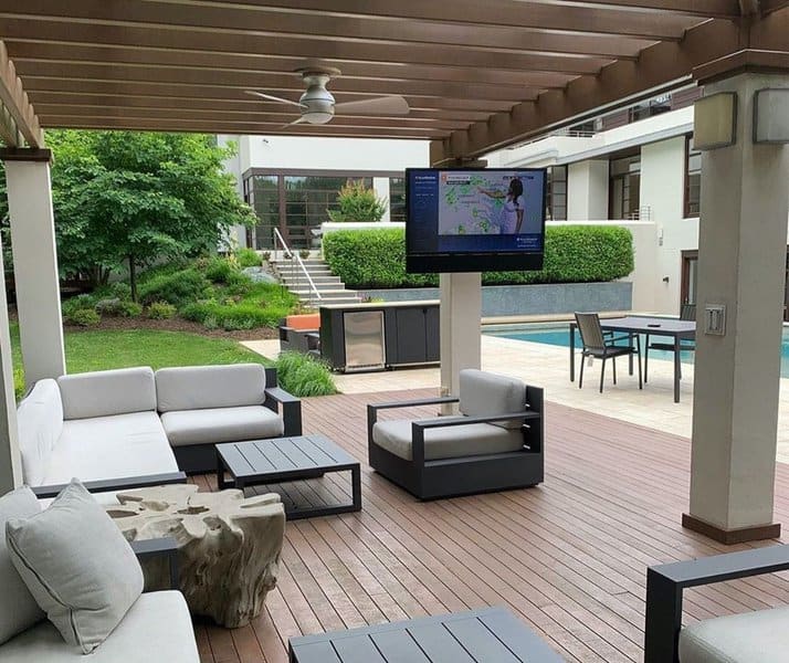 Modern outdoor lounge with pergola, stylish furniture, poolside views, and a mounted TV for ultimate relaxation and entertainment