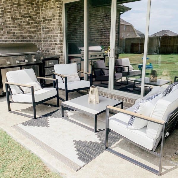 Modern patio with white chairs, gray table, and a grill beside a brick house